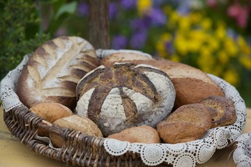 Different fresh bread on old wooden table. Lots of fresh bread in a basket and a board with flour on a wooden table