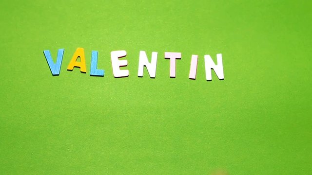 Wood characters of different colors arranged in a word Valentine's day on a green background with hand slide
