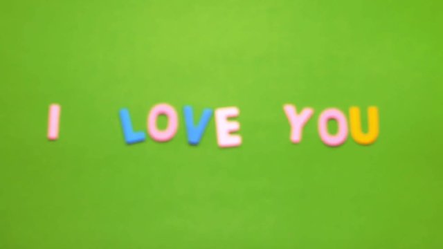 Wood characters of different colors arranged in a word I love you on a green background with blur effect
