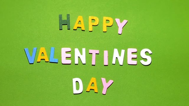 Wood characters of different colors arranged in a word happy valentine's day on a green background with blur effect
