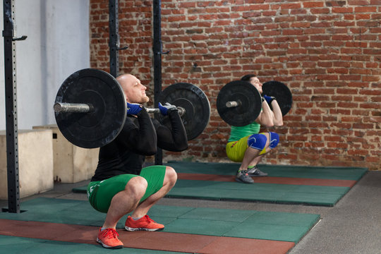 Athletic men doing workout with barbells at the gym