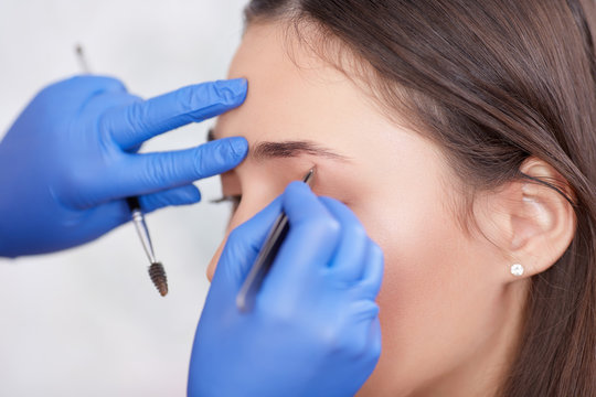 Professional in gloves plucking eyebrows for female.