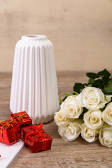 White roses with gift boxes and vase. Valentines day concept with notepad. Love design. Wooden rustic board.