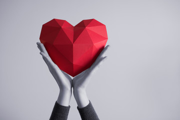 Two female hands holding red polygonal paper heart shape. Tonned image