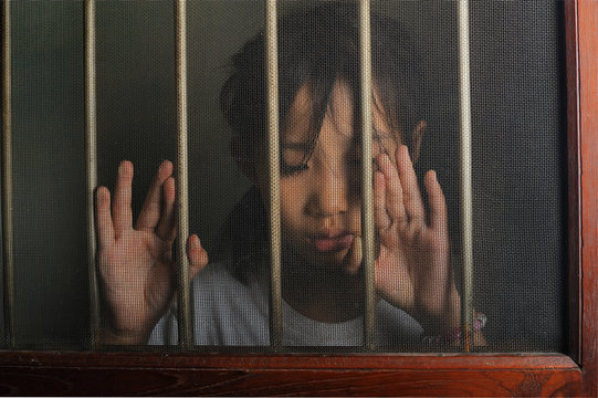 sad asian child standing behind the wire screen window.  Unhappy
