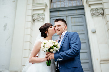 Wedding. Wedding day. Wedding couple. Bride kisses the groom sitting on his hands against a white castle