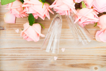 Pink blooming fresh valentines day roses buds on wood with two champagne glasses close up