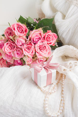 Female dress and jewellery with freah roses bouquet and present box on chair