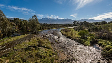 Fototapeta na wymiar Shallow stream in Corsica with snow capped mountains in distance