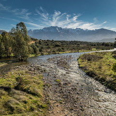 Shallow stream in Corsica with snow capped mountains in distance
