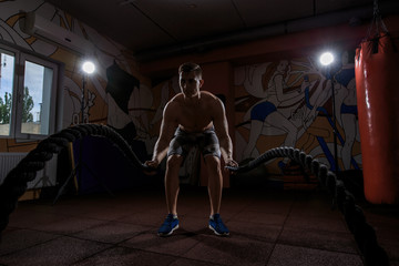 Obraz na płótnie Canvas Young man working out with battle ropes at crossfit gym