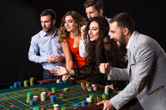 Group of young people behind roulette table on black background