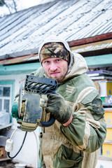 Obraz premium Man angry in military clothes. Work picked up a power saw. Man scares chainsaw an opponent in the street in winter