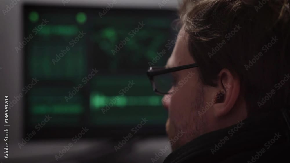 Poster close up of hacker in eyeglasses looking in monitor and hacking computer system. male thief trying t