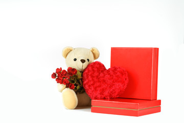 Valentine's day concept : Teddy bear hugging bunch of roses together with heart-shaped pillow and red boxes isolated on white background