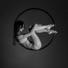 Young beautiful slim dancer on aerial hoop posing on a black studio background