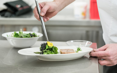 Koch in Restaurant garniert Salat und Pastete mit Blüten