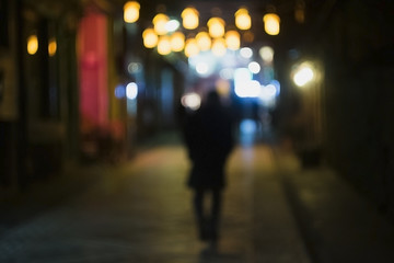 A lonely man is walking in a shiny street. Which is illuminated with chinese lanterns.
