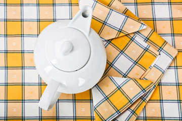 top view of a white teapot on a yellow checkered tablecloth