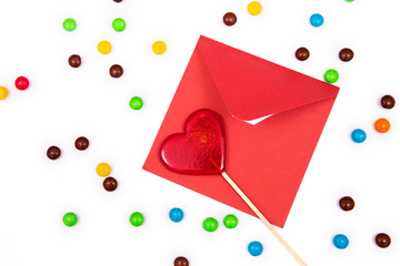 Gift for Valentines day. Red envelope and red lollipop in the shape of a heart on the white background with colorful button-shaped chocolates.