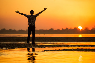 Fototapeta premium Silhouette of happy man show hand up for success on the beach at sunset time.