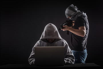 Terrorist  attack  hacker with gun work at laptop.