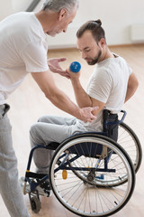 Involved disabled man exercising with his coach in the gym