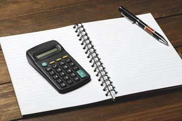 Office supplies with pen and calculator on brown wooden table.