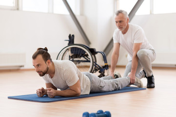 Peaceful physical therapist stretching the disabled patient in the gym