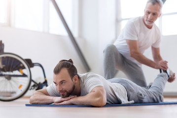 Aged bearded father stretching his disabled son in the gym