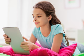 smiling girl with tablet pc lying in bed at home