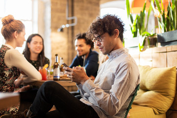 man with smartphone and friends at restaurant