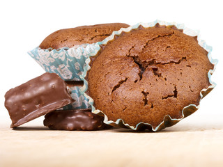 Muffins and chocolate sweets. Fresh baked cakes in paper baking dish with cracked surface on wooden board.