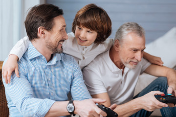 Cute positive boy standing behind his father and grandfather