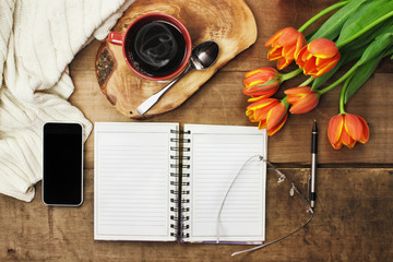 Overhead shot a bouquet of an open book, cell phone, coffee and flowers over a wood table top ready...