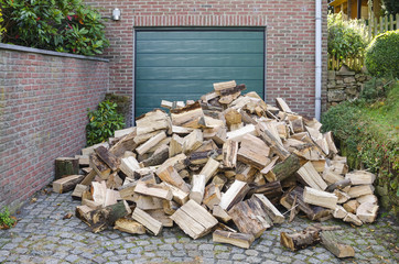 Supply of cut firewood, dumped on a garage driveway of a small house.
