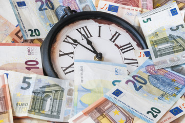 Fuenf Minuten vor zwoelf Uhr / Euro Geldscheine und eine Uhr, die Zeiger stehen fuenf Minuten vor zwoelf.