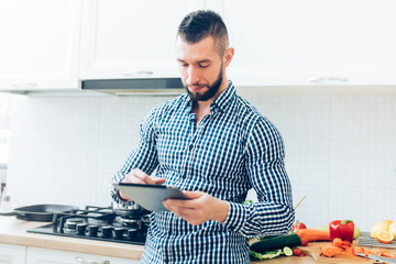 Handsome male working in kitchen, looking up on the internet receipes. Details of modern cook working with tablet