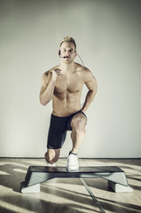 Young aerobics male coach shirtless leaning on step teaching class, looking at camera