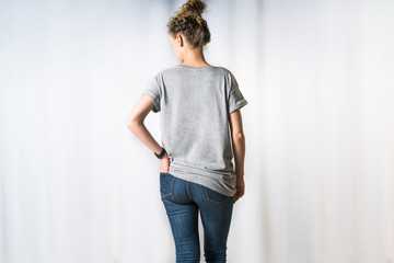 Rear view of young woman, dressed in light gray T-shirt and blue jeans, standing for light...