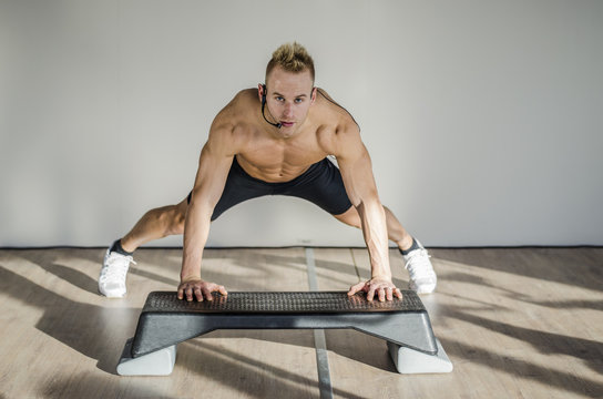 Young aerobics male coach shirtless leaning on step teaching class, looking at camera