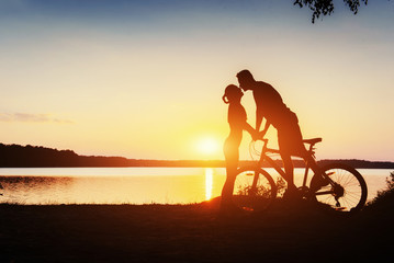 Obraz na płótnie Canvas couple on a bicycle at sunset by the lake