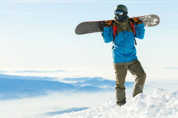 Fototapeta na wymiar Snowboarder standing at the very top of a mountain and holding snowboard behind his back