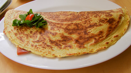 Pancake stuffed with tomato, cheese and green salad on white plate. 