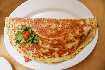 Pancake stuffed with tomato, cheese and green salad on white plate. Top view