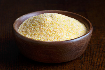 Cornmeal polenta in brown wooden bowl isolated on dark wood.