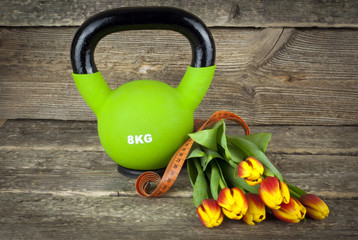 Modern kettlebells and tied with a measuring tape bouquet of tulips flowers on a wooden background....