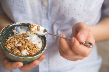 Young woman with muesli bowl. Girl eating breakfast cereals with nuts, pumpkin seeds, oats and...