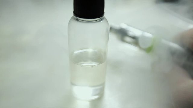 Bottle with liquid and flavor for electonic cigarette stay on the table. A lot of steam for background.