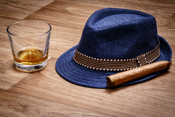 blue hat with cigar and expensive drink of whisky or rum on wooden floor